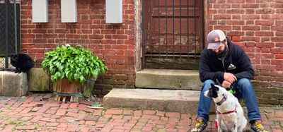 Jason Quintin Sitting on a stoop with his dog not looking at the camera and black cat on the far left of the frame